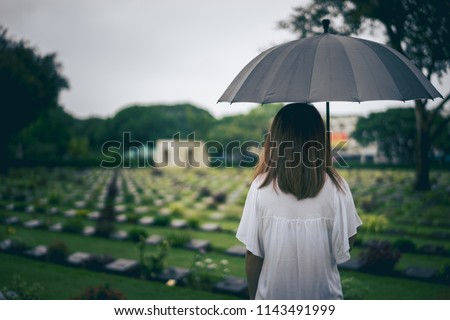 Young woman holding black umbrella mourning at cemetery