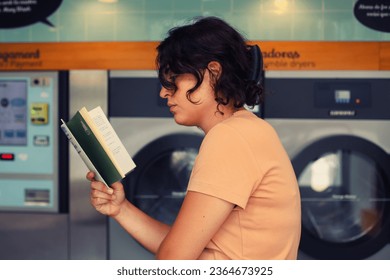 Young woman holding a book in front of a washing machine at the laundromat - Powered by Shutterstock