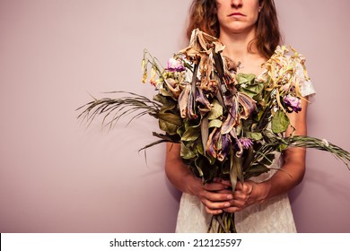 A young woman is holding a bouquet of dead flowers