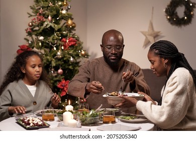 Young Woman Holding Bowl With Food While Her Husband Taking Piece Of Meat During Family Dinner On Christmas Day