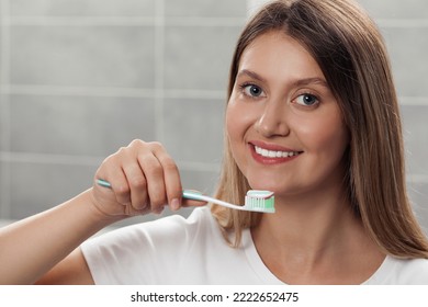 Young Woman Holding Brush With Toothpaste In Bathroom