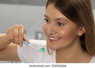 Young Woman Holding Brush With Toothpaste In Bathroom