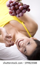 Young woman holding bunch of grapes, smiling, portrait