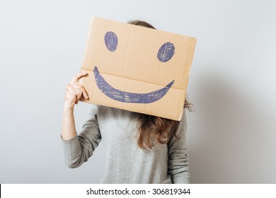 Young woman holding cardboard smiley. On a black background.