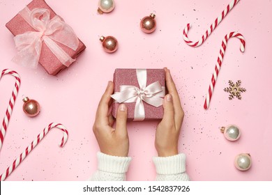 Young woman holding Christmas gift on pink background, flat lay