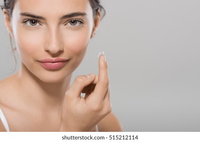 Young woman holding contact lens on index finger with copy space. Close up face of healthy beautiful woman about to wear contact lens. Eyesight and ophthalmology concept.