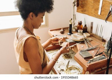 Young woman holding crafts tool and ornament piece in workshop. Female designer examining ornament piece before giving final touch by crafts tool in the workshop.