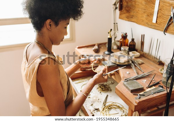 Young woman holding crafts\
tool and ornament piece in workshop. Female designer examining\
ornament piece before giving final touch by crafts tool in the\
workshop.