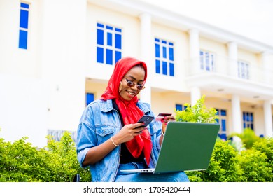 Young Woman Holding Credit Card Using Laptop At Home Shopping Due To Isolation Of Staying At Home  In Quarantine. Hipster Shopping Online With Mobile Phone Using Credit Card