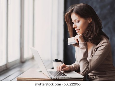Young woman holding credit card and using laptop computer. Businesswoman working at home. Online shopping, e-commerce, internet banking, spending money, working from home concept