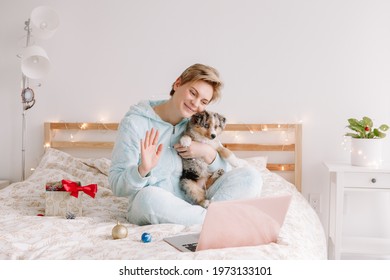 Young Woman Holding Cute Puppy Dog And Call Friends Family On Video Chat. Pet Owner Celebrating Christmas Holiday Alone. Distant Remote Holiday Celebration Online On Internet At Coronavirus.