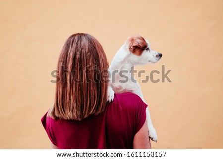 young woman holding cute small jack russell dog on shoulder. yellow wall background