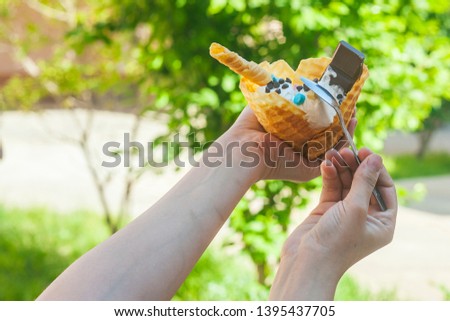 Young woman holding delicious ice cream with waffle during a picnic at nature. Summer food concept. Young adult eating yummy ice cream with a stick on a bright summer day