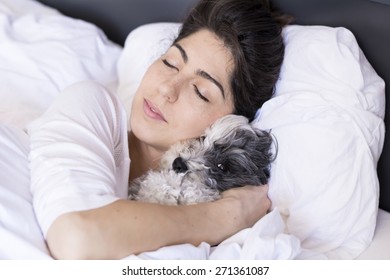 young woman  is holding a dog while laying on a bed. Horizontal shot.