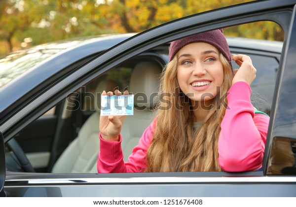 Young woman\
holding driving license near open\
car