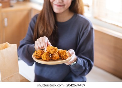 A young woman holding and eating fried chicken in the kitchen at home