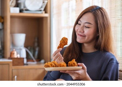 A young woman holding and eating fried chicken in the kitchen at home - Powered by Shutterstock