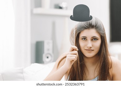 Young woman is holding a fake mustache on a stick in front of her face, making a funny expression for a photo booth style picture - Powered by Shutterstock