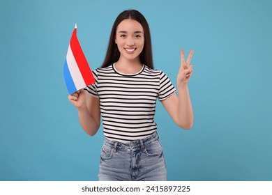 Young woman holding flag of Netherlands on light blue background