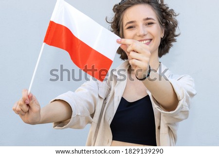 Young woman holding flag of Poland over gray background and looking at camera. Happy female student, learning Polish.