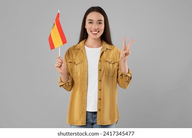 Young woman holding flag of Spain on light grey background