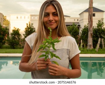 Young woman holding fresh basil leaves from the kitchen garden, at sunset.  - Powered by Shutterstock