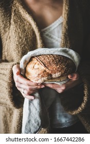 Young woman holding freshly baked healthy wheat Swedish bread round loaf in tpwel in hands, selective focus