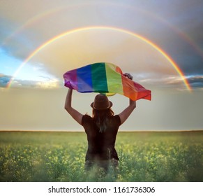 Young woman holding gay rainbow flag in the field