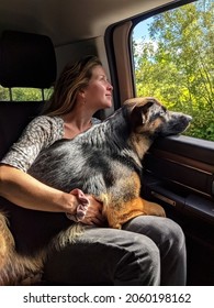 Young Woman Holding German Shepherd Dog Looking Out A Truck Window While Traveling