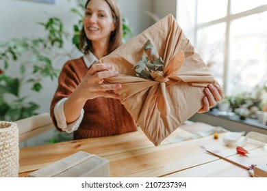 Young woman holding gift box packing in fabric furoshiki style with dried eucalyptus. Eco friendly package concept. Selective focus.