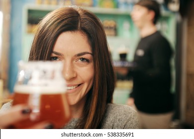 Young woman holding glass of beer with man serving in the background