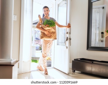 Young woman holding grocery shopping bag with vegetables. Girl entering into home.                       - Powered by Shutterstock