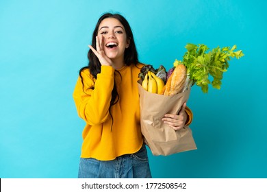 Young Woman Holding A Grocery Shopping Bag Isolated On Blue Background Shouting With Mouth Wide Open