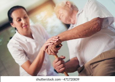 Young woman holding hand of old man with walking stick