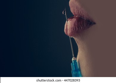 young woman holding with hand syringe with liquid drop near sexy lips and mouth on grey background making botox injection