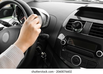 Young woman holding hands on steering wheel and air freshener hanging in car, closeup