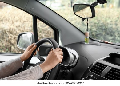 Young woman holding hands on steering wheel and air freshener hanging in car