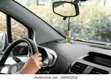 Young woman holding hands on steering wheel and air freshener hanging in car