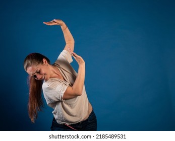 Young Woman Holding A Heavy Item. Blue Background. Woman Showing A Product. Photo For Advertising. Woman Holding Something Above Her Head. Woman Feeling Heavy Weight