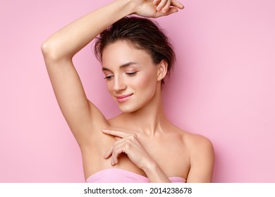 Young woman holding her arm up and showing clean underarm. Photo of smiling woman with smooth skin after epilation on pink background. Beauty concept