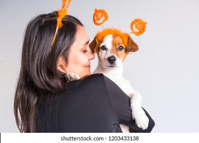 Young Woman Holding Her Cute Small Dog Over White Background. Matching Pumpkin Diadems. Halloween Concept. Indoors