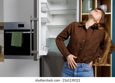 Young Woman Holding Her Stomach While Standing Near Refrigerator In The Kitchen