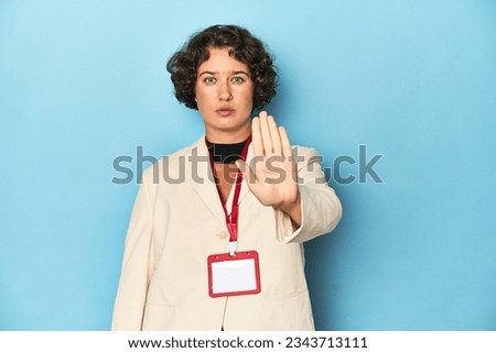 Young woman holding identification card for event standing with outstretched hand showing stop sign, preventing you.