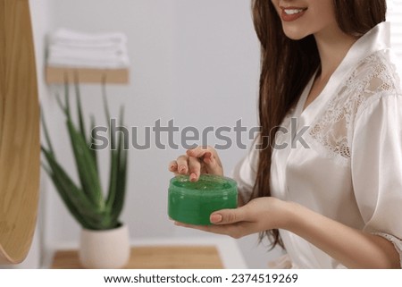 Young woman holding jar of aloe hair mask indoors, closeup. Space for text