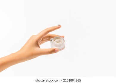 Young Woman Holding Jar Of Cream And White Cosmetic Cream On Her Index Finger On White Background. Beauty Skin Care Creamy Product Sample. BB, CC Cream Texture. Makeup Foundation. Copy Space 