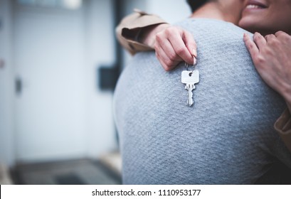 Young woman holding keys hugging husband in front of their new home after buying real estate
