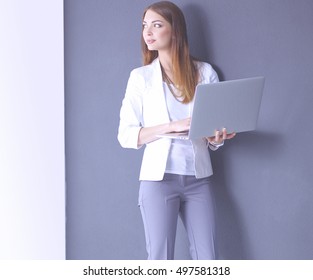 Young woman holding a laptop, standing on gray background - Shutterstock ID 497581318