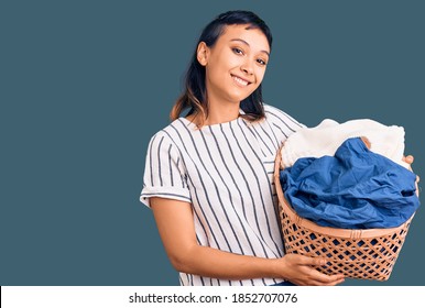 Young Woman Holding Laundry Basket Looking Positive And Happy Standing And Smiling With A Confident Smile Showing Teeth 