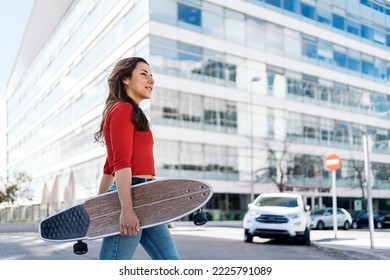 Young woman holding longboard in the street and looking at front.