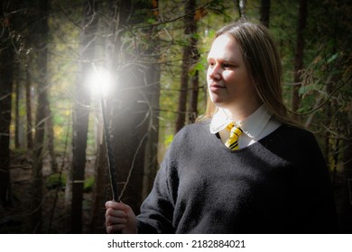 Junge Frau, die erstaunt einen Zauberstab hält und sieht, der Licht von seiner Spitze wegwirft, im Herbstwald, um einen Zauber zu werfen 